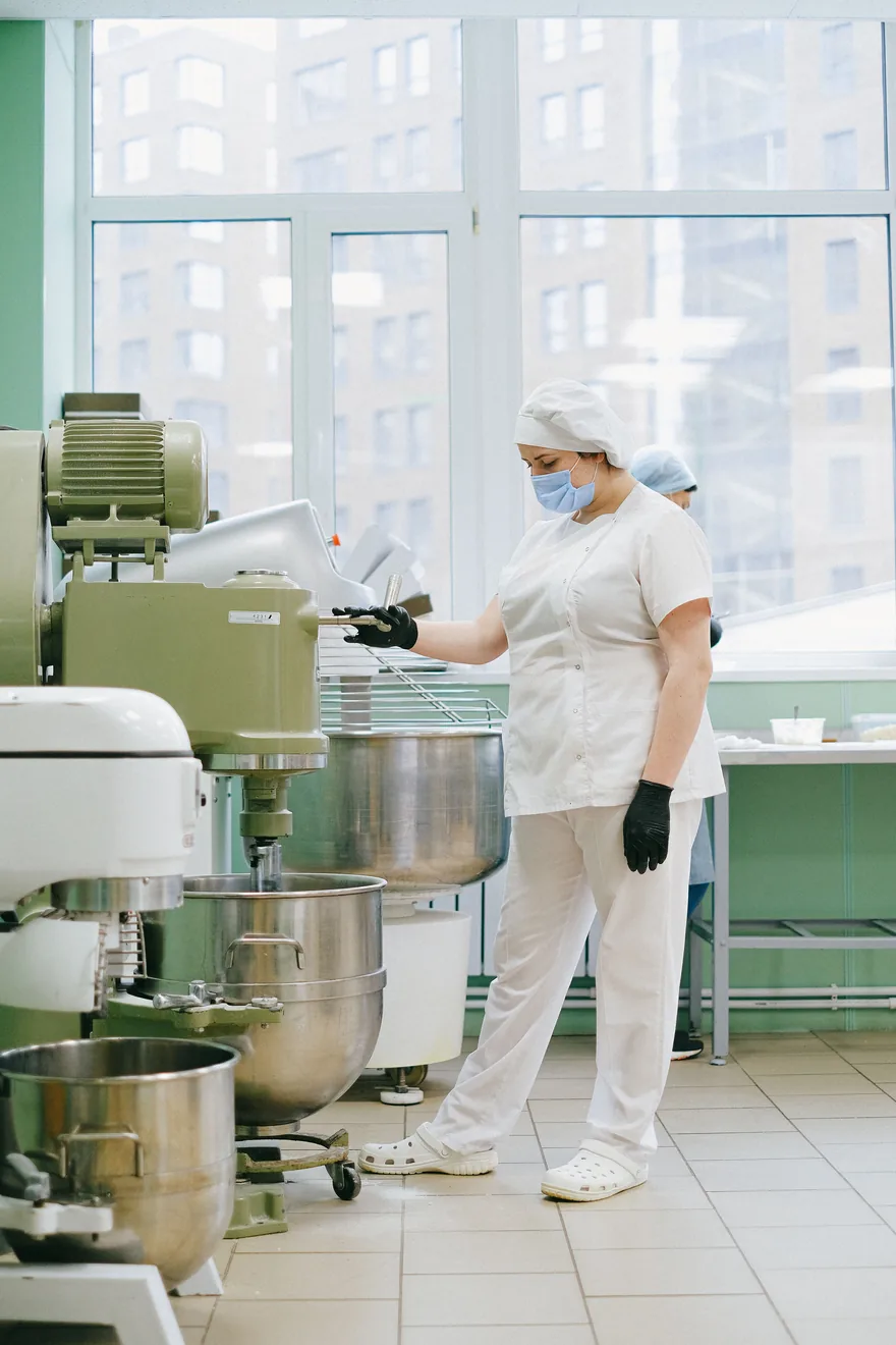 Operaria en una planta de producción de alimentos manipulando equipos industriales en un entorno certificado